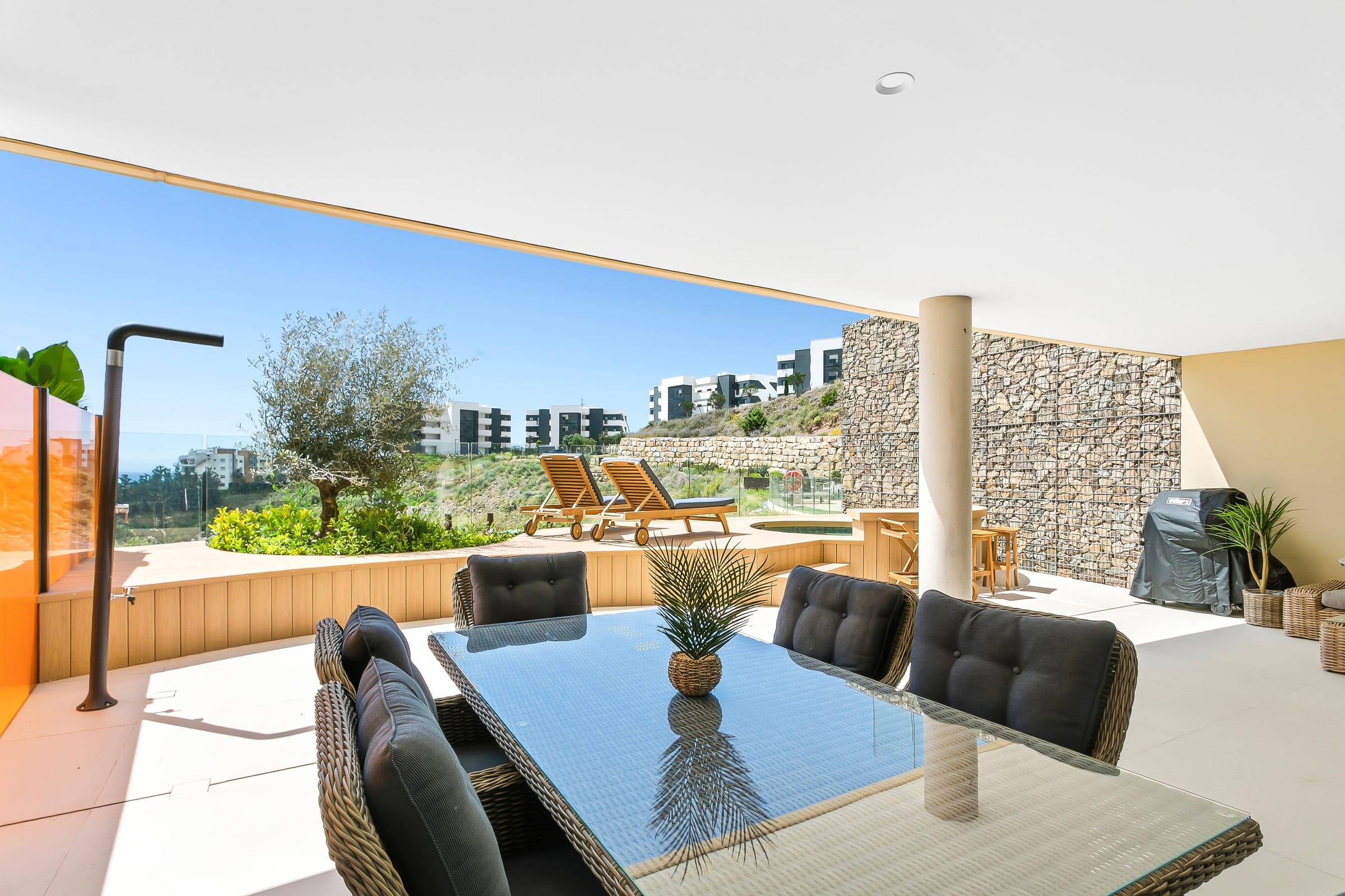 Covered terrace with dining table, garden and sun loungers at a rental home we manage